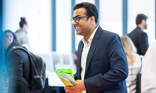 A male student smiles and engages with others at a career fair event.