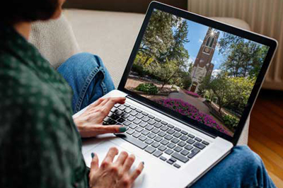 A close-up image of a woman using a laptop computer while a picture of the Beaumont Tower at Michigan State University displayed on the screen.