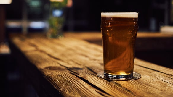 A glass of beer rests on top of a wood bar