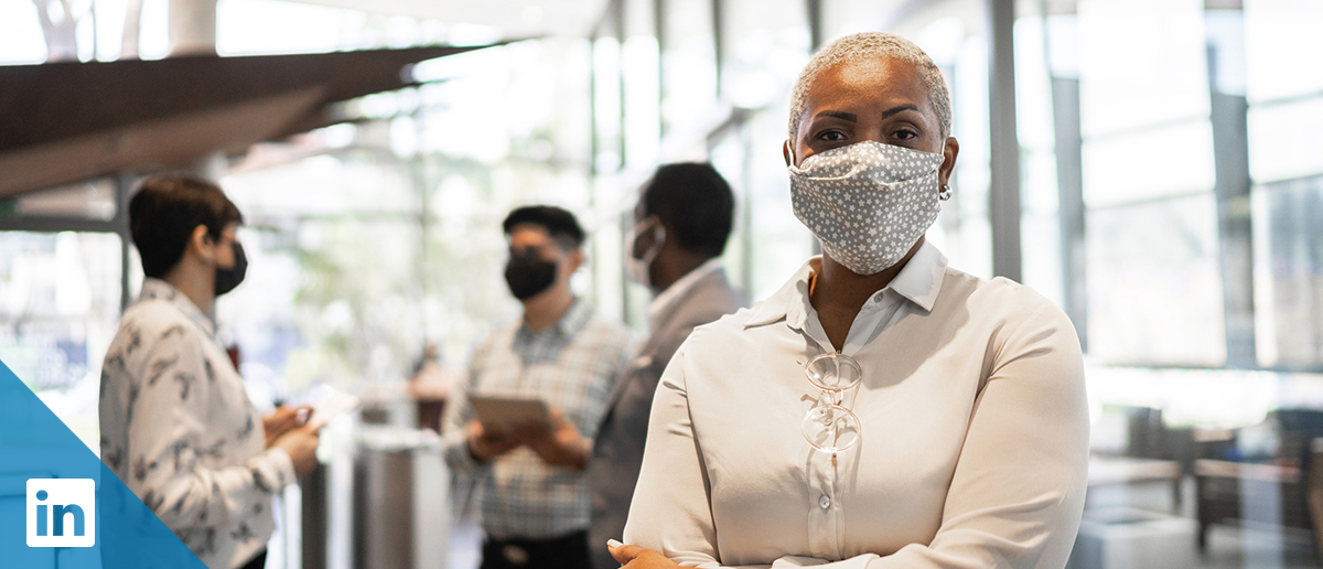 Woman wearing a face mask in the foreground, with three people in face masks conversing in the background