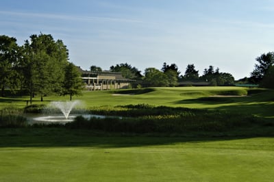 A fountain sprays water upwards on Forest Akers golf course, and the Henry Center for Executive Development can be seen in the distance