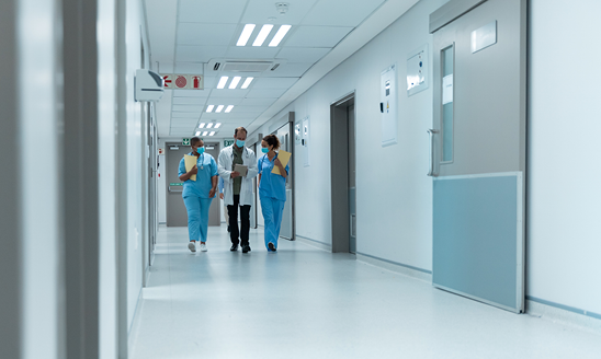 Three health care professionals walk down a wide hospital hallway