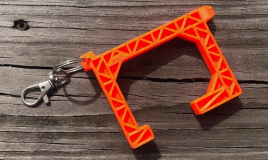 The Spartan-designed and 3D-printed No Touch Tool with keychain shown laid on a wood surface.