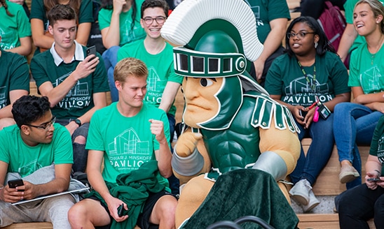 A male student bumps fists with MSU's mascot, Sparty, at the 2019 Minskoff Pavilion ribbon cutting event.