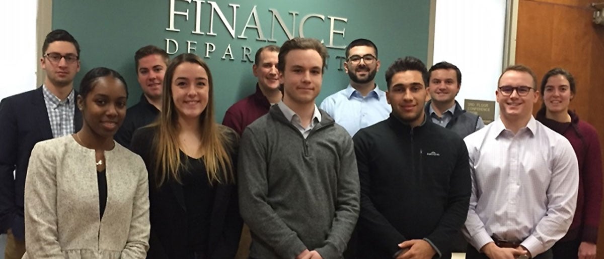 Student venture capitalists stand next to each other and pose for a picture in front of the Finance Department sign