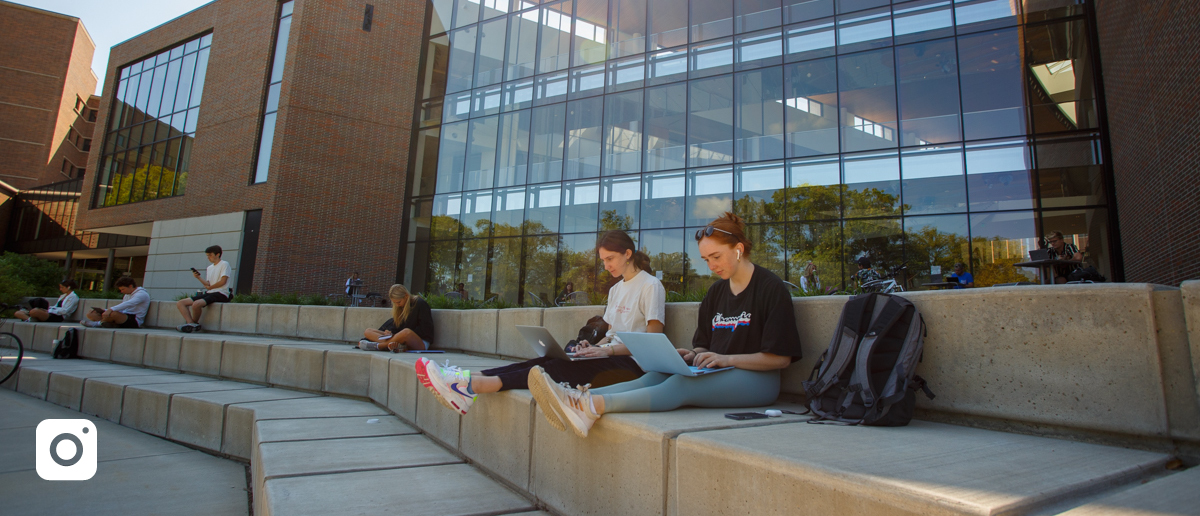 Students with laptops and backpacks sitting outside the Minskoff Pavilion