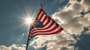 The United States flag flies in front of sun and clouds