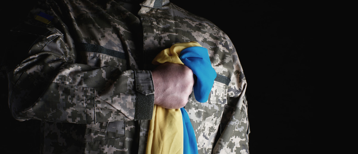 A Ukraininan soldier holds the blue and yellow flag in a fist over his heart