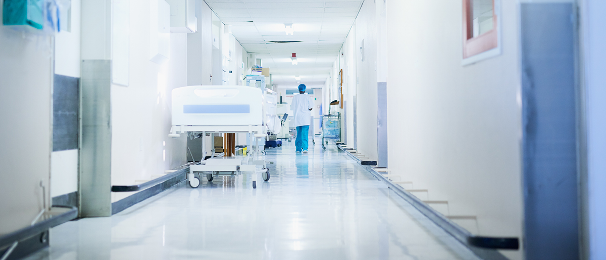 A healthcare worker walks down an otherwise empty hospital corridor