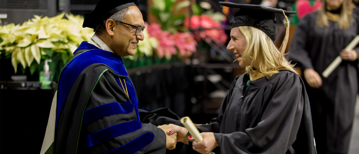 Dean Sanjay Gupta shakes hands and congratulates a young woman who is graduating with an advanced degree from the Broad College.