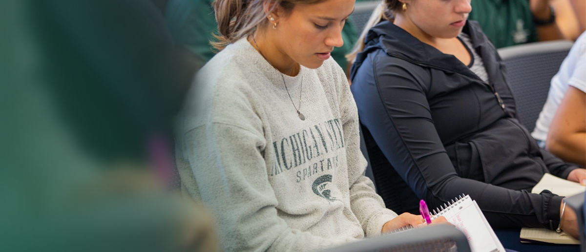 A close-up image of female students taking notes in class at Michigan State University.
