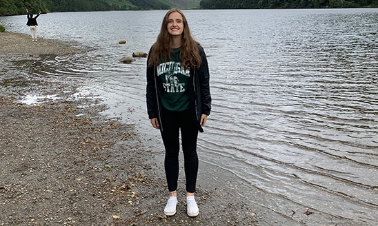 Valerie McNamara, an international relations and business freshman, standing outdoors on a study abroad trip wearing a green and white MSU t-shirt.